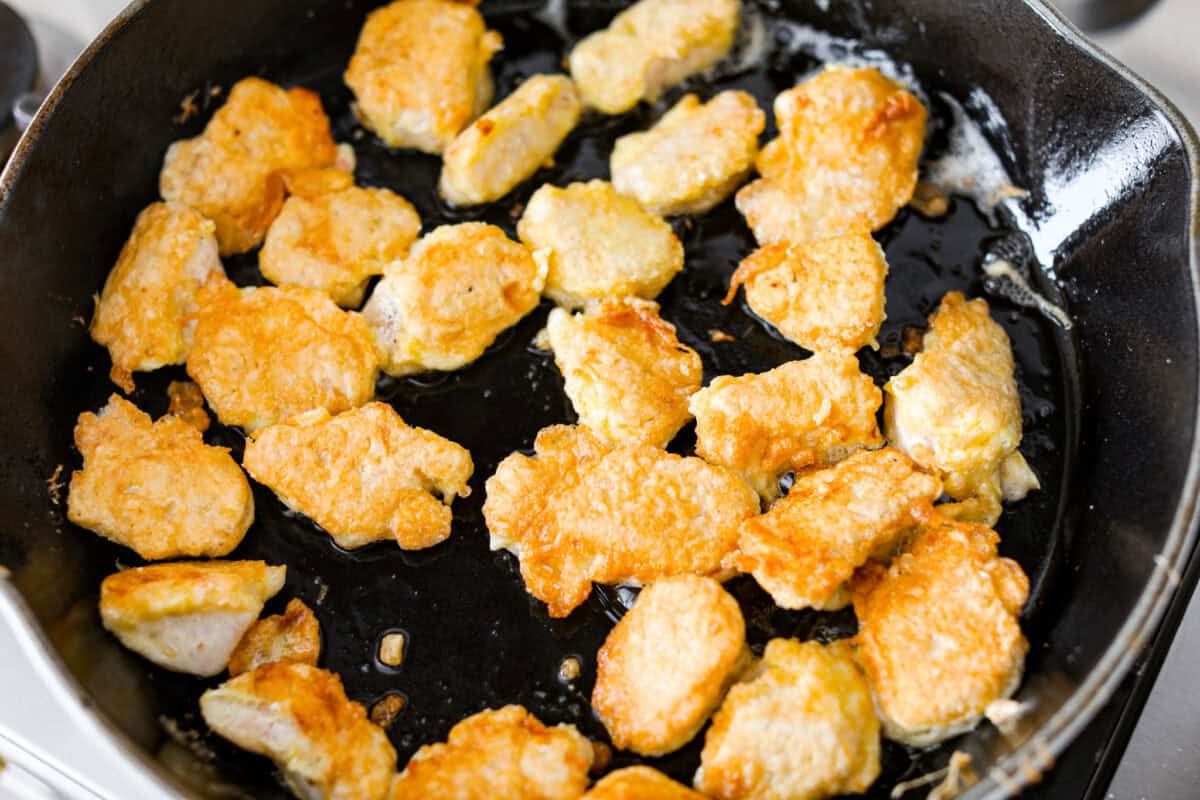 Coated chicken pieces cooking in a skillet. 