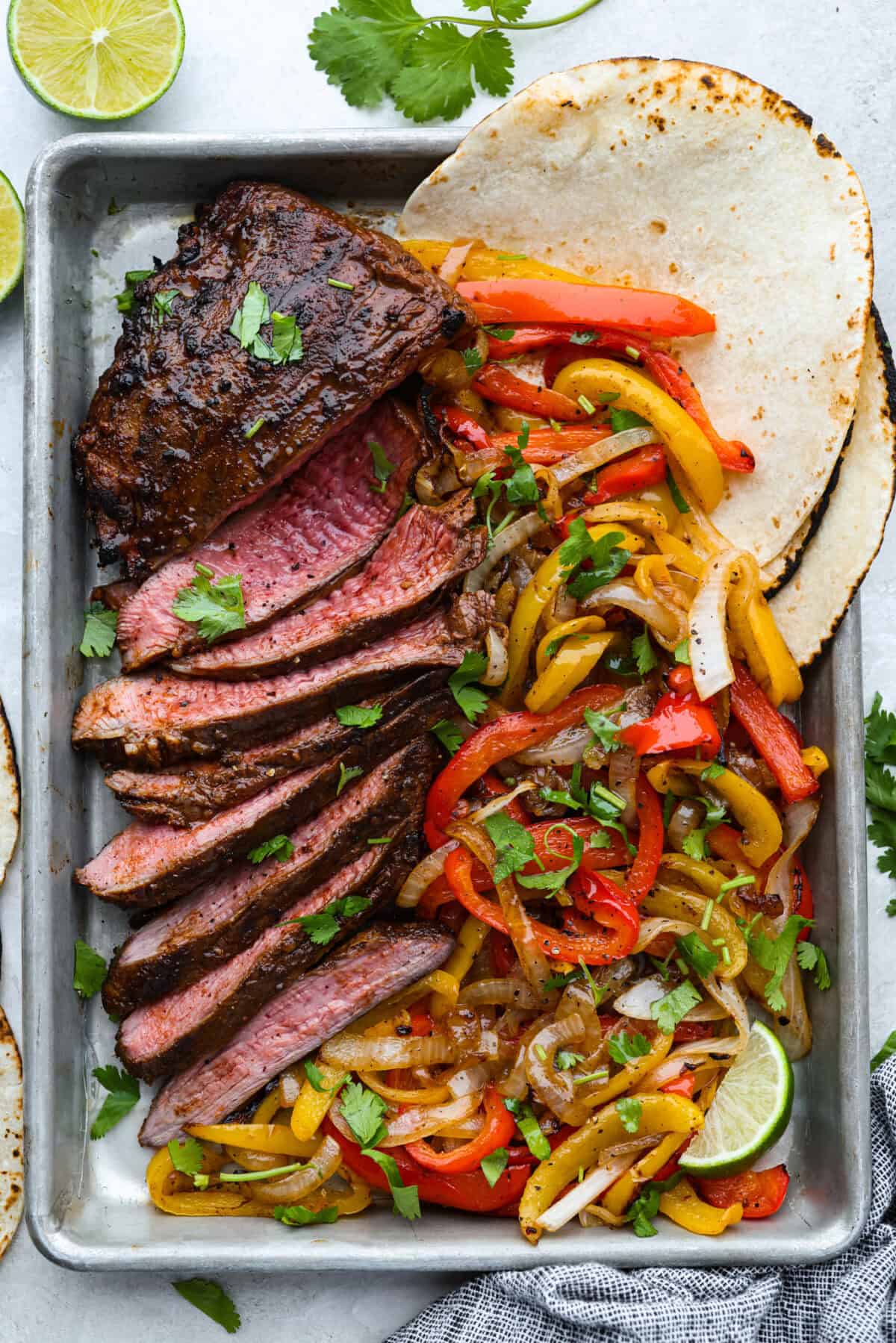 Sheet pan with grilled steak fajitas and veggies and tortillas. 