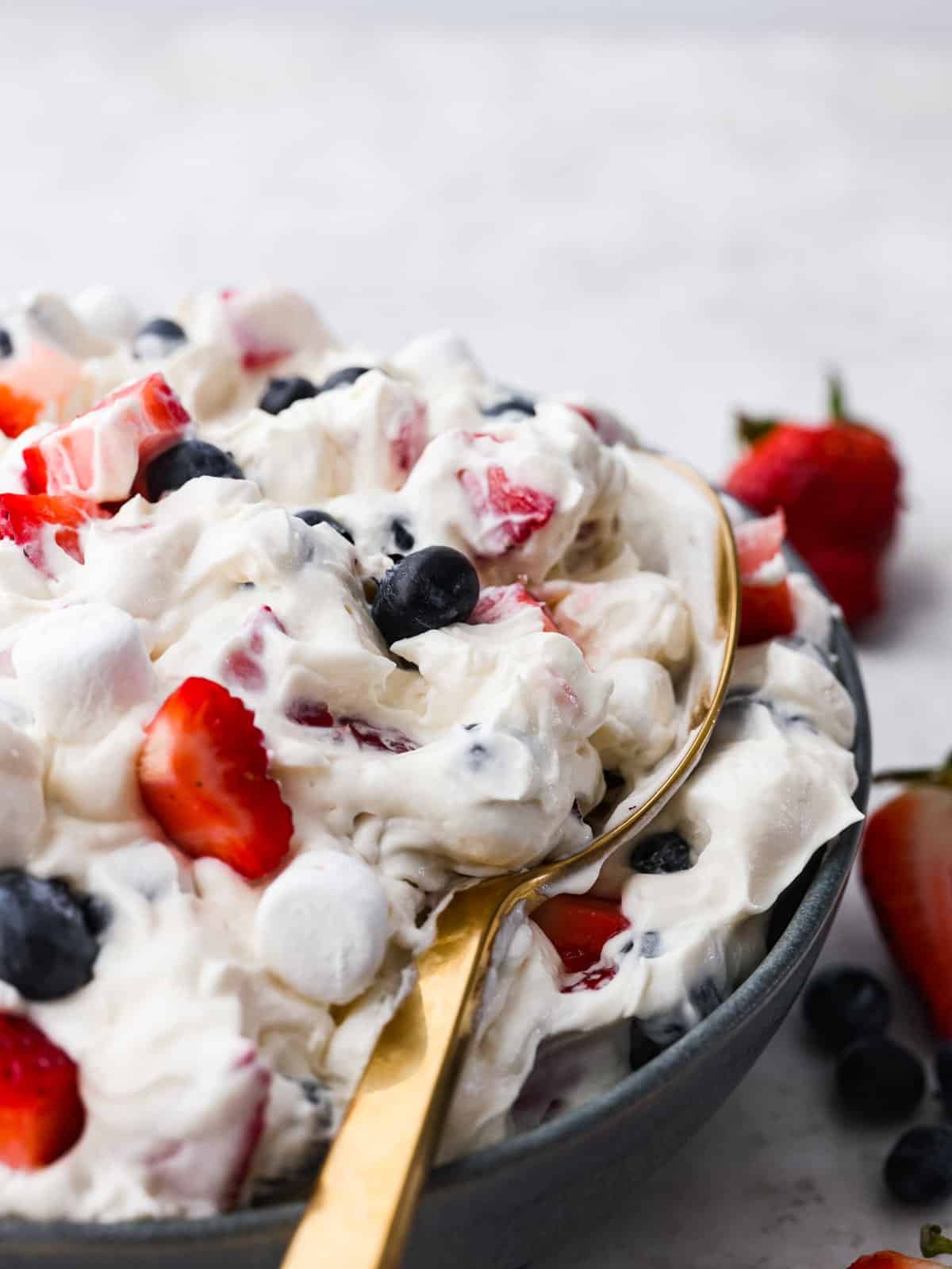 Red White and Blue Cheesecake salad being scooped up with a gold spoon.