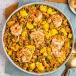 Bowl of pineapple fried rice with small bowls of scallions and cashews.