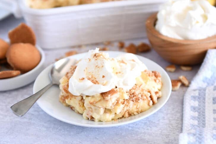 Serving of banana pudding on white plate topped with whipped cream.