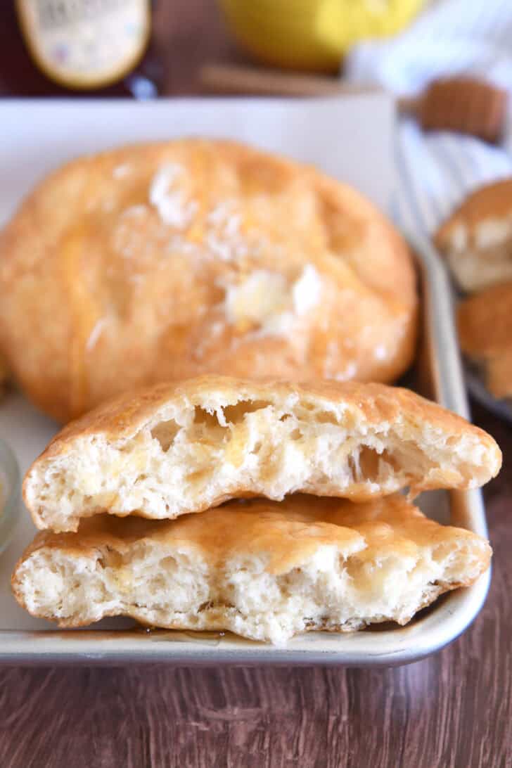 Piece of cooked fry bread cut in half on tray with honey.