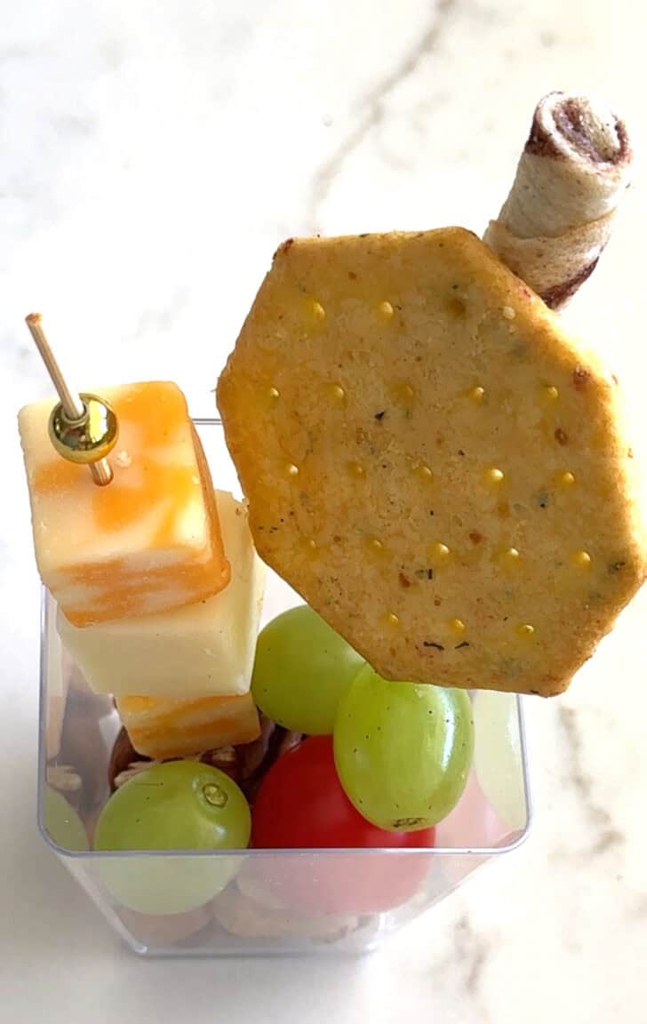 Square plastic cup with cracker, cheese skewer, and pirouline.
