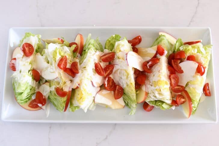 White platter with iceberg wedges, tomatoes, sliced apples, and blue cheese dressing.