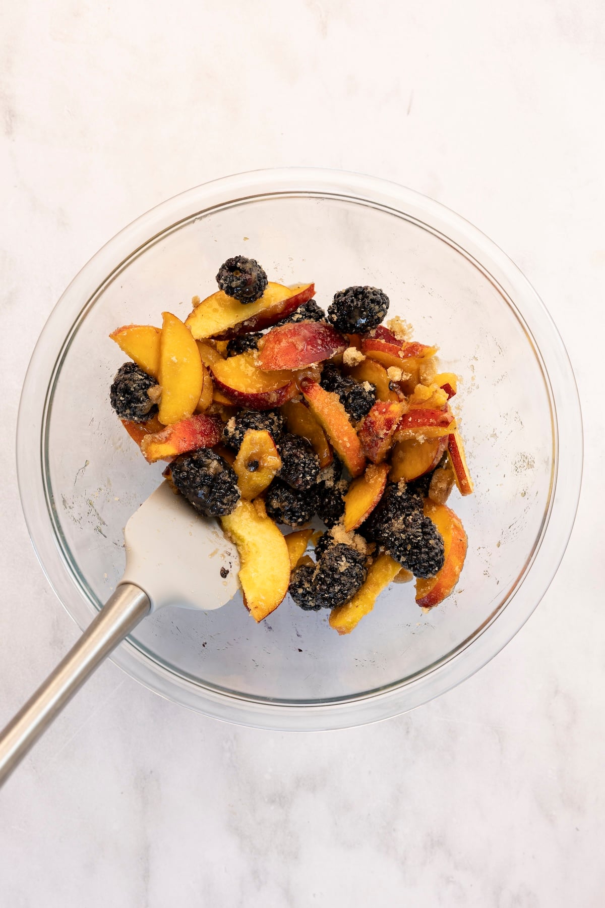 medium glass bowl with peaches, blackberries and brown sugar mixed together 