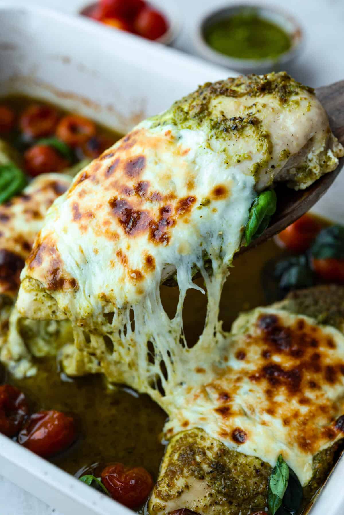 Someone lifting out a cheesy baked pesto chicken breast from the baking dish.