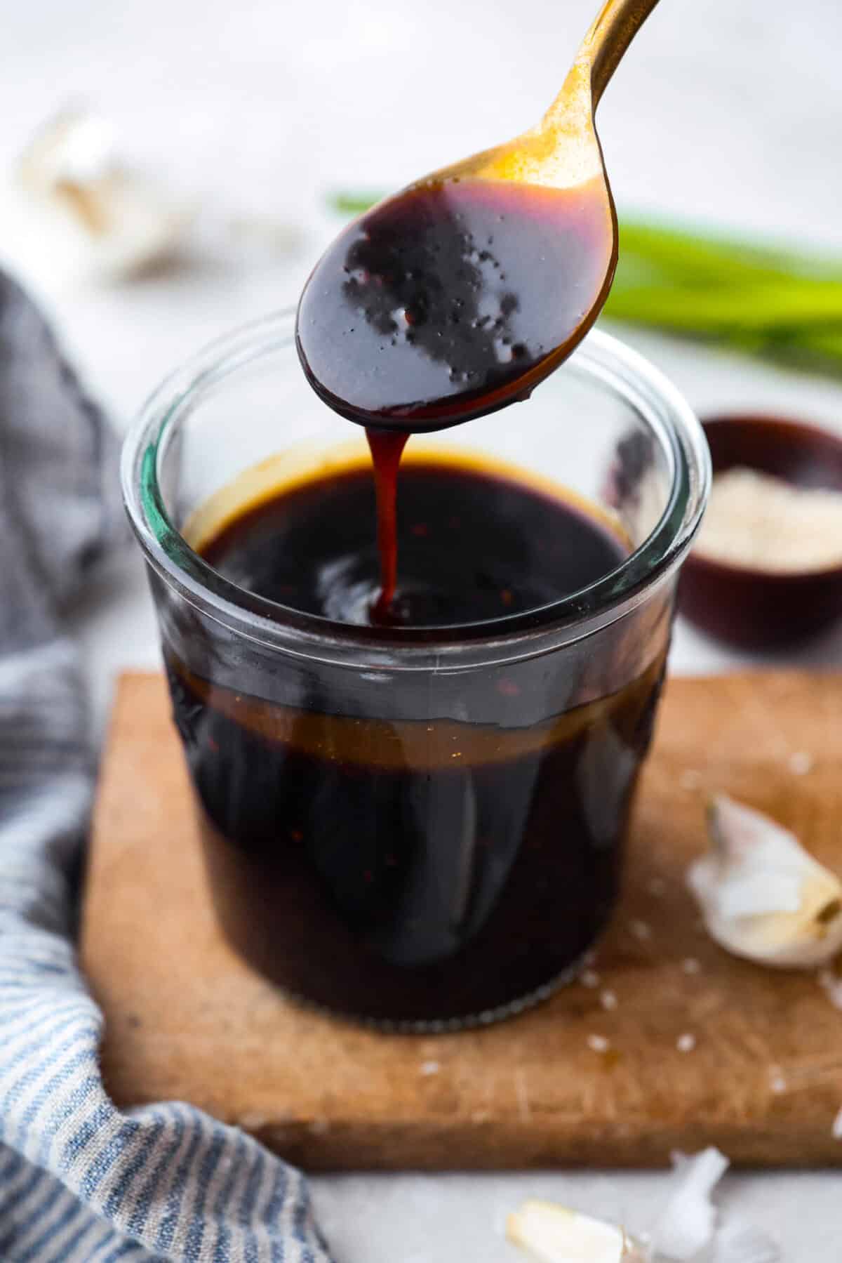 Jar of homemade teriyaki sauce and someone dripping some from a spoon. 