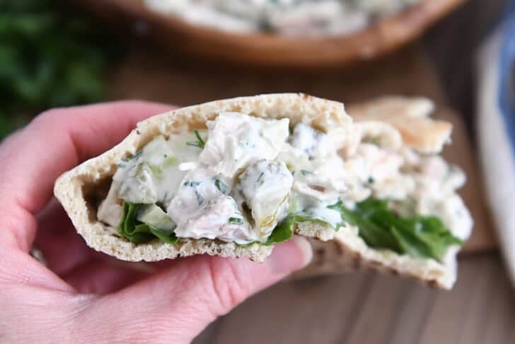 Holding half of a pita bread stuffed with dill pickle chicken salad.