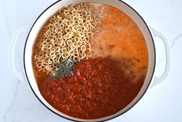 Deep skillet with small pasta, milk, red sauce, basil and oregano.