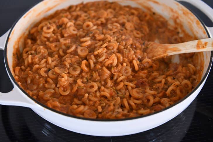 Cooking pasta in red sauce with shredded zucchini in deep skillet.