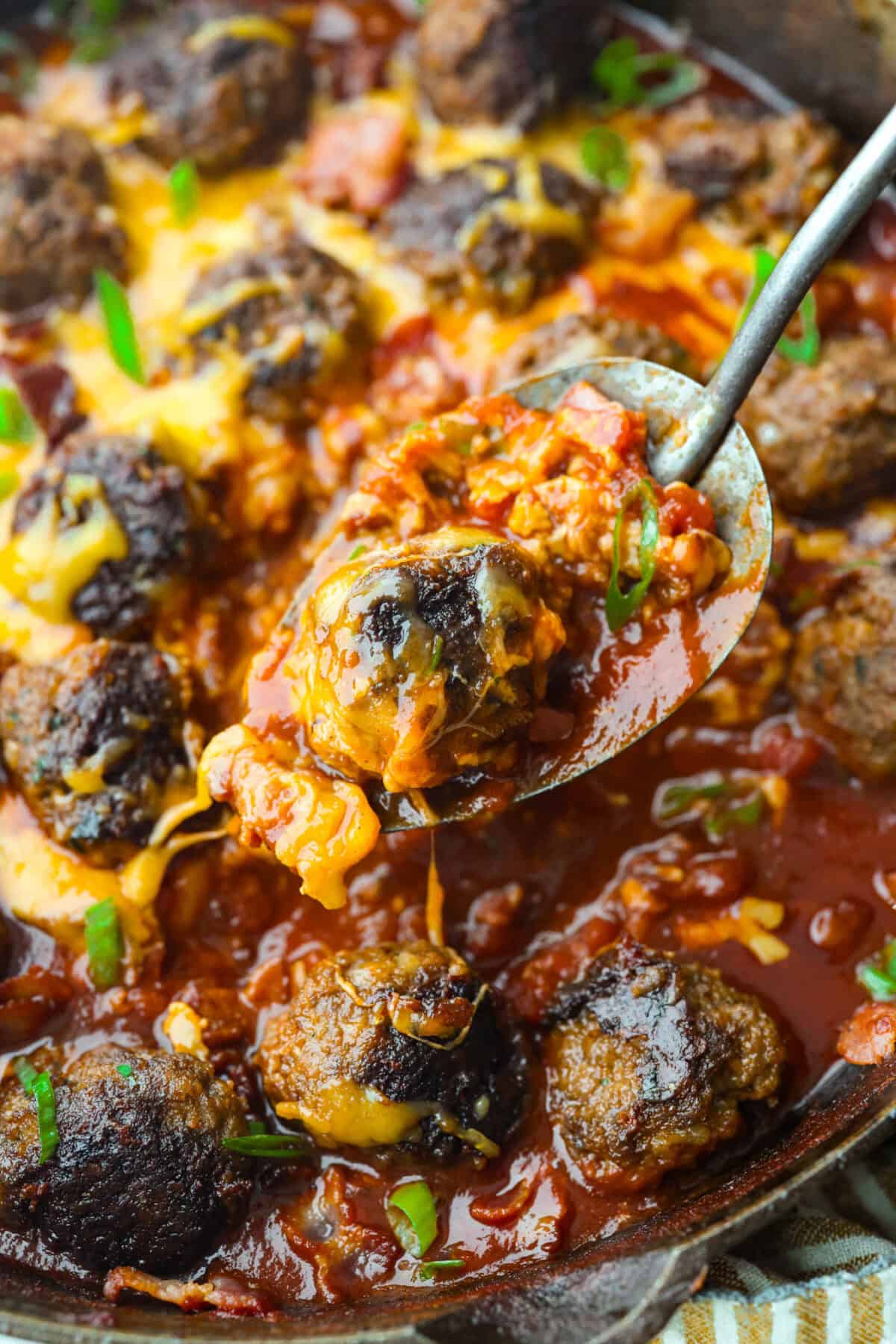Close up shot of a spoon with a cowboy meatball and the cheesy sauce. 