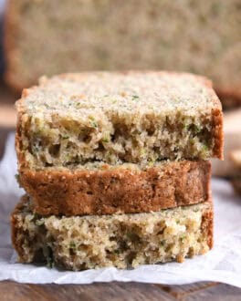Three half slices of zucchini bread stacked on piece of parchment paper.
