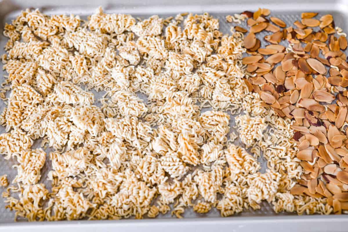 Toasted broken up ramen noodle pieces and almond slices on a baking sheet.
