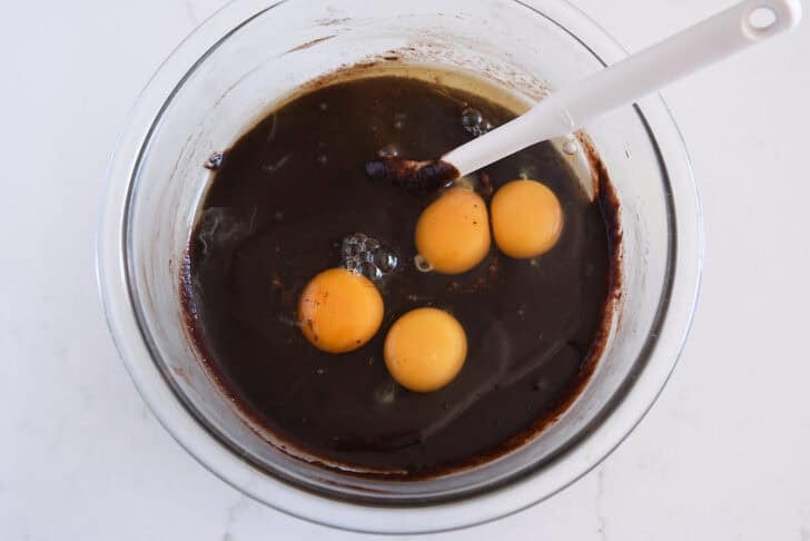 Glass bowl with melted chocolate batter and eggs.