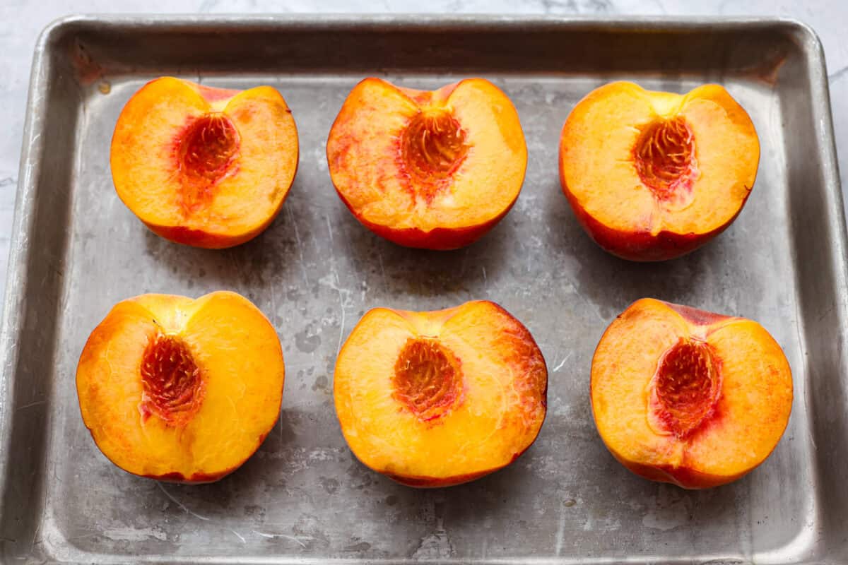 Peaches cut in half, pits taken out, and lined up on a baking sheet. 