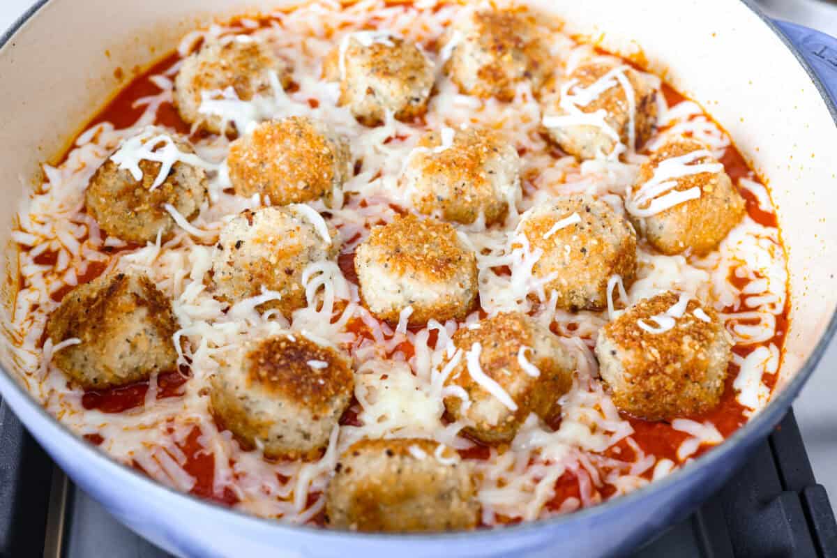 Browned meatballs, marinara sauce and cheese added to the skillet ready to be baked in the oven.