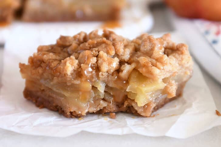 One caramel apple crumble bar on white parchment paper with bite taken out.