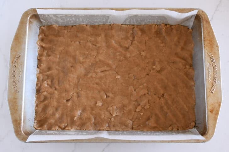 Metal 9X13-inch pan with parchment and unbaked crust pressed into the bottom.