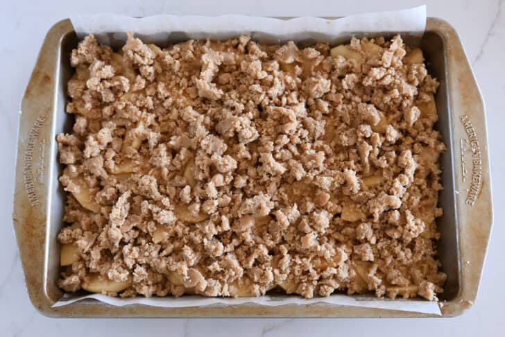 Metal 9X13-inch pan with unbaked layers of crust, sliced apples, and buttery streusel.