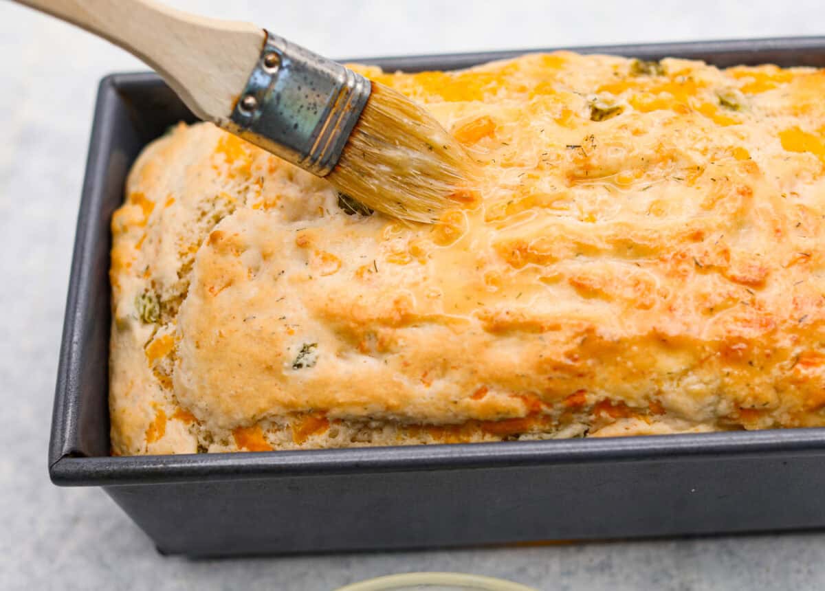 Someone spreading the dill pickle butter on top of the baked loaf. 
