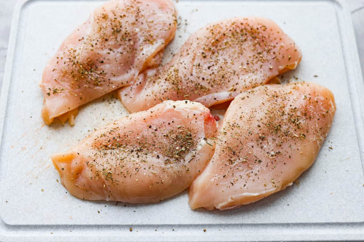 Chicken breasts on a cutting board and seasoned. 