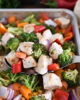 Serving spoon with cooke chicken, broccoli, carrots, bell peppers and red onions.