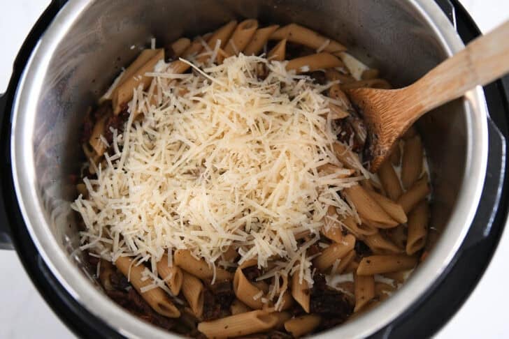 Shredded Parmesan cheese in Instant Pot with cooked pasta, cream and sun-dried tomatoes.