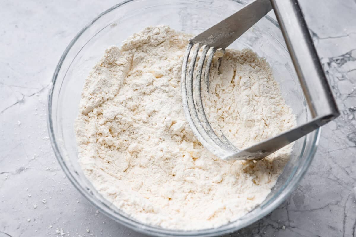 Flour, baking powder, salt and cold butter being combined with a pastry blender. 
