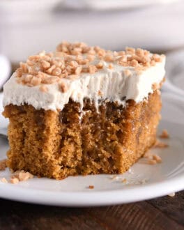 Square of pumpkin caramel poke cake with bite taken out and topped with frosting and toffee bits.