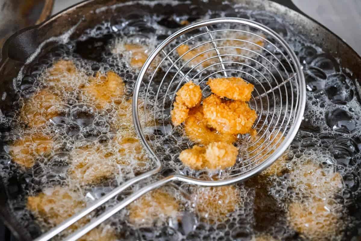 Someone lifting out fried shrimp out of the oil. 
