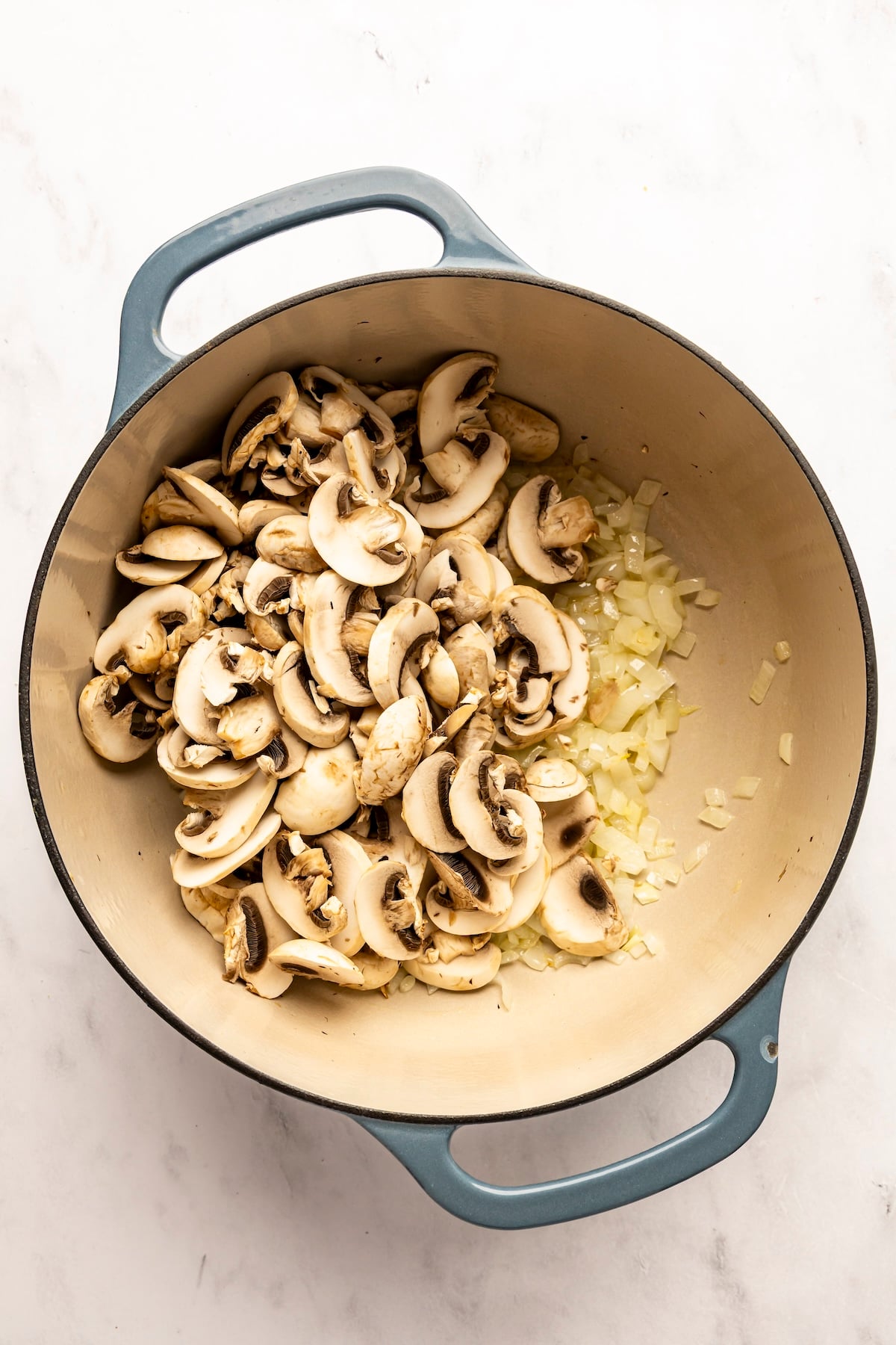 dutch oven with sliced mushrooms added to sauteed onions