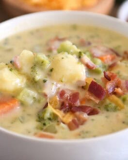 Spoon scooping spoonful of loaded broccoli cheese bacon soup in white bowl.