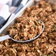 Sheet pan with baked pumpkin pecan granola with deep metal spoon scooping up granola.