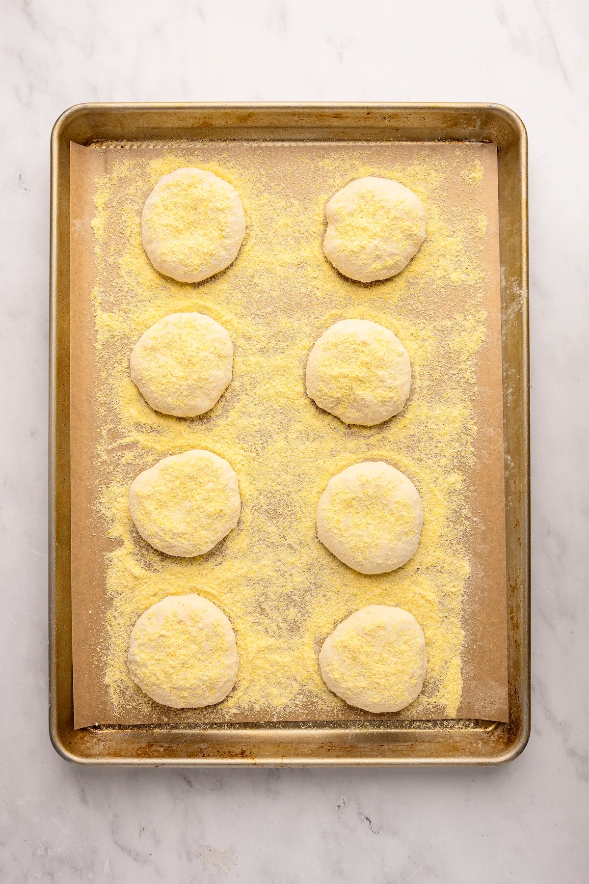 Parchment-lined baking sheet with English muffin rounds covered with cornmeal 
