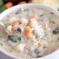 White soup bowl with spoon scooping up creamy soup with carrots, gnocchi, spinach, sausage and freshly grated Parmesan cheese.